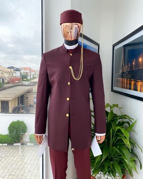 Une saharienne bordeaux à boutons dorés, un gilet intérieur, une chemise à col roulé, un chapeau, un pantalon.